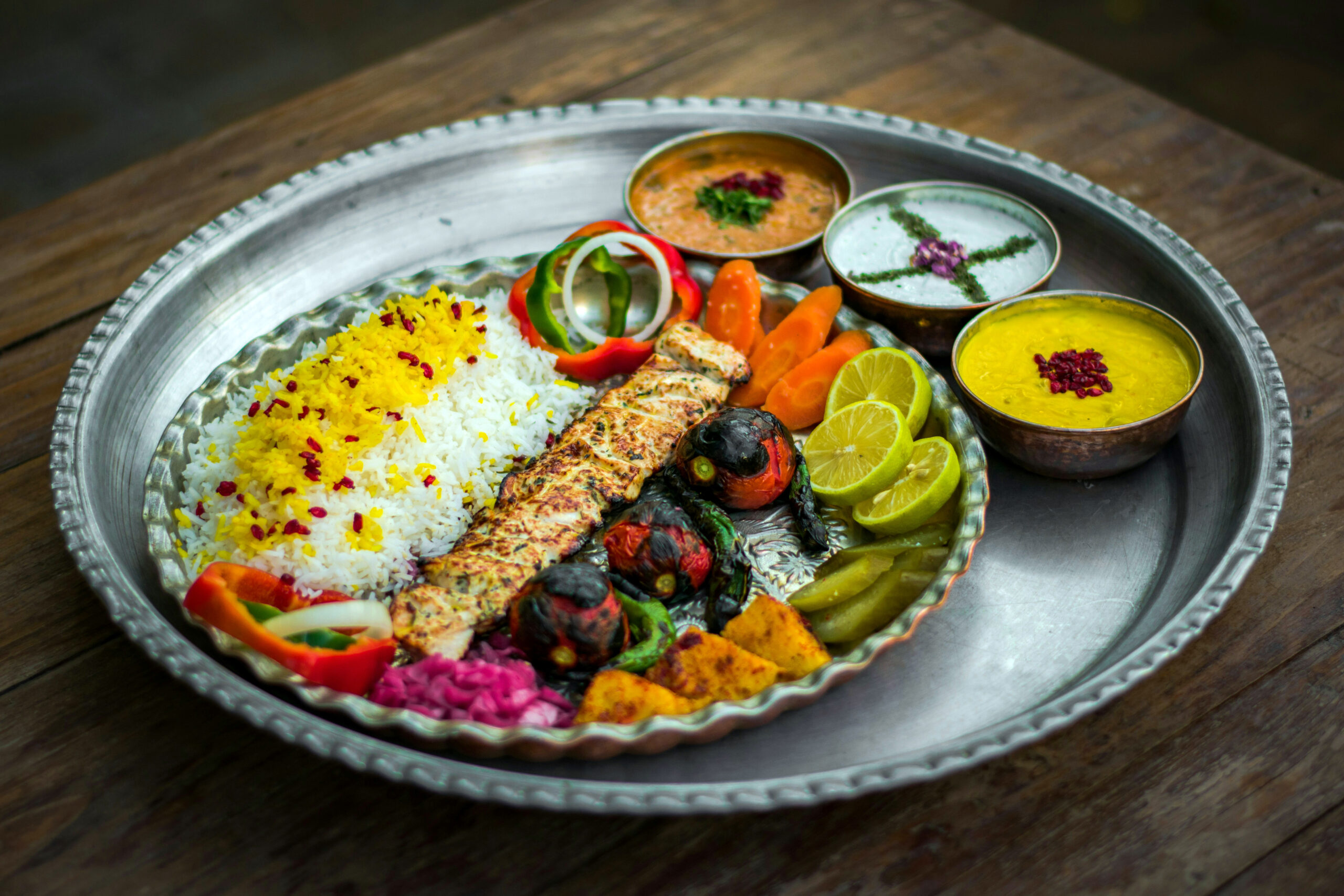 Perzisch gerecht met saffraanrijst, kipkebab, gegrilde tomaat en yoghurt op een koperen dienblad – World Wide Kitchen